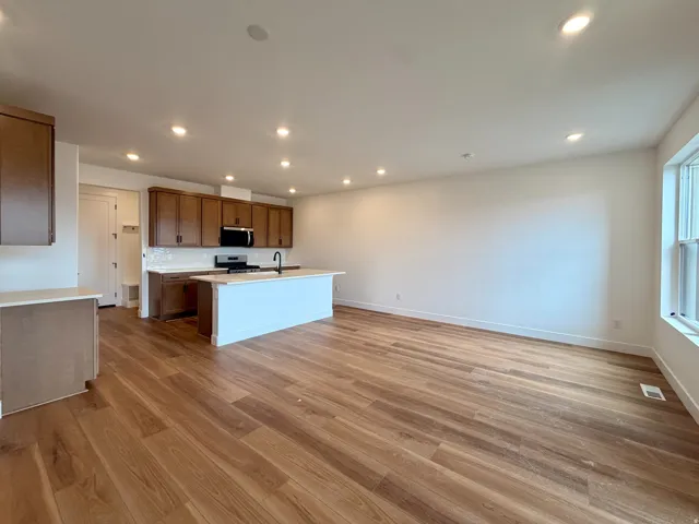 Open-concept living area with wood-finish flooring, recessed lighting, and a kitchen featuring dark wood cabinetry and a white subway tile backsplash