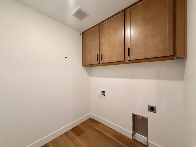Wood-finish flooring, overhead cabinetry with dark hardware, ceiling-mounted exhaust fan, and dedicated appliance hookups