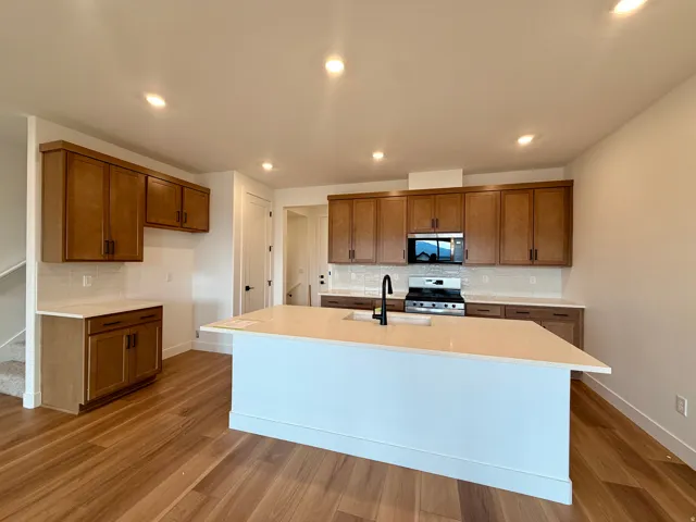 Kitchen featuring wood-finish flooring, recessed lighting, wood cabinetry, a center island with a sink, and a tile backsplash