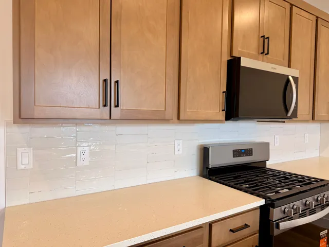 Updated kitchen featuring natural wood cabinetry with black hardware, white subway tile backsplash, stainless steel gas range with multiple burners, and light-toned countertops with ample workspace