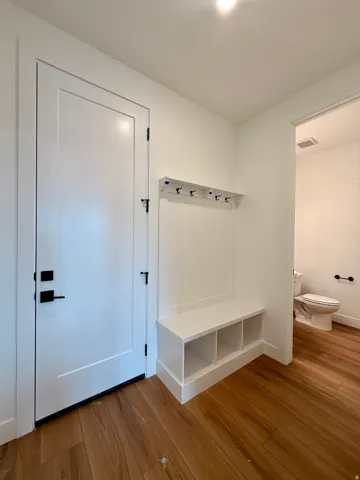 Wood-finish flooring, built-in storage bench with cubbies, wall-mounted coat rack, white interior doors with dark hardware, and a well-lit interior