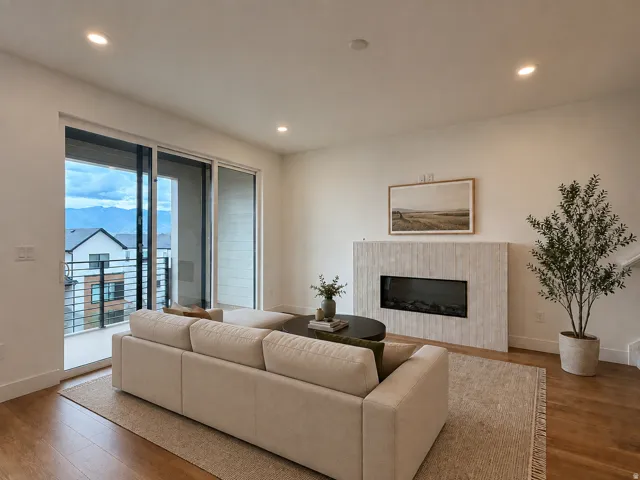 Recessed lighting, wood-finish flooring, a contemporary fireplace with a textured surround, and sliding glass doors leading to a balcony with metal railings*This picture has been virtually staged using AI*