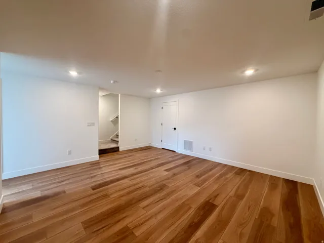 Wood-finish flooring with white trim, recessed lighting, and a white paneled door with matte black hardware