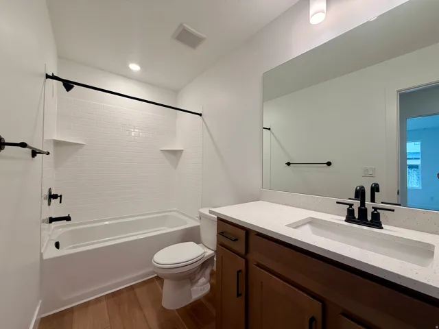 Secondary bathroom featuring a wood-finish vanity with dual-sink white quartz countertop, matte black hardware, and large framed mirror