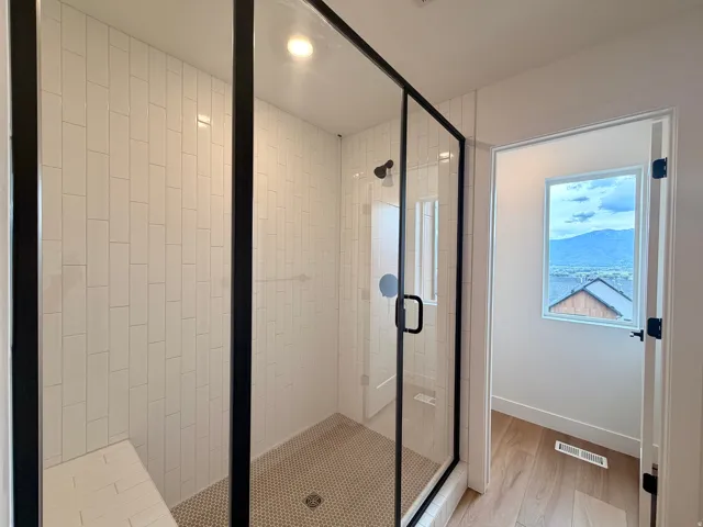 Owner's bathroom with walk-in shower with black-framed glass enclosure, white rectangular tile walls, and a built-in bench