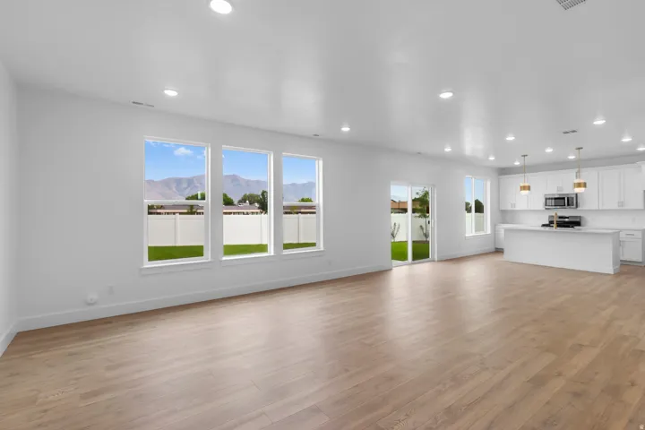 Expansive open-concept space featuring wood-finish flooring, a contemporary kitchen with white cabinetry, a large island, and stainless steel appliances