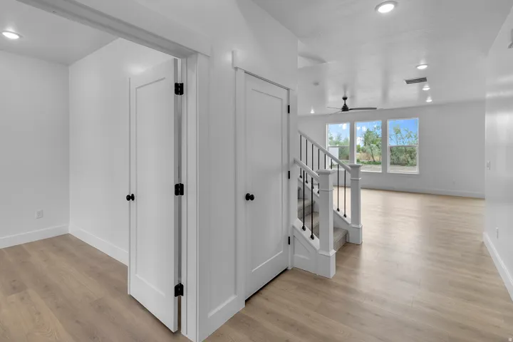 Recessed lighting, wood-finish flooring, white paneled doors, staircase with black metal balusters, and multiple windows revealing exterior foliage