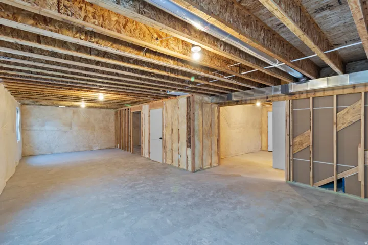 Unfinished basement with exposed ceiling joists, concrete flooring, and framed interior walls
