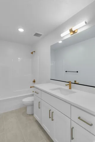 Bathroom featuring a white vanity with integrated sink, gold-tone fixtures, a tub/shower combination, and tiled flooring