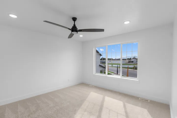 Neutral tone carpeting, white painted walls, recessed ceiling lighting, a contemporary ceiling fan, and a multi-pane window