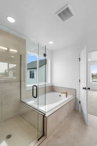 Glass-enclosed shower with herringbone tile floor, separate soaking tub with gold-tone fixtures, and large format tile flooring
