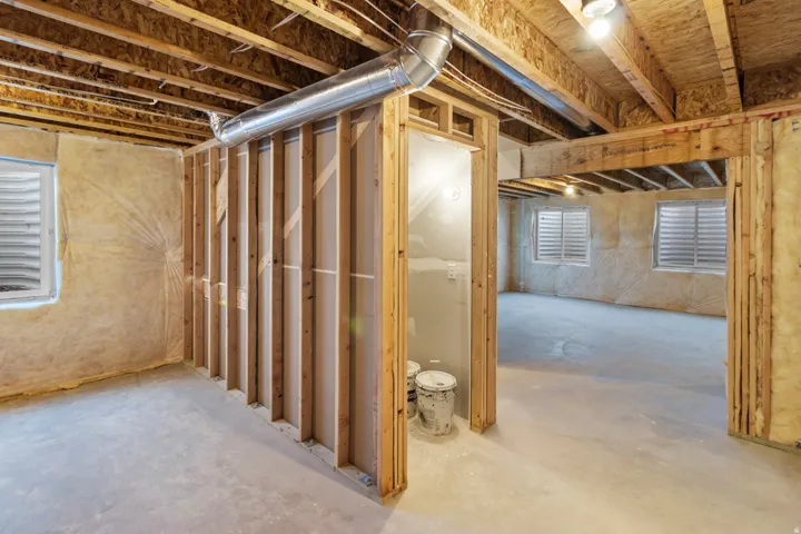 Unfinished basement with exposed wood framing, concrete flooring, multiple egress windows, and visible ductwork