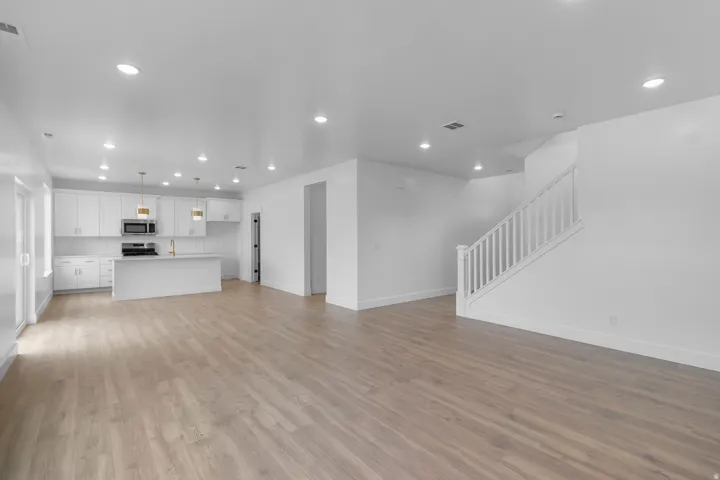 Spacious open-concept layout with wood-finish flooring, white cabinetry, a kitchen island, and recessed lighting throughout