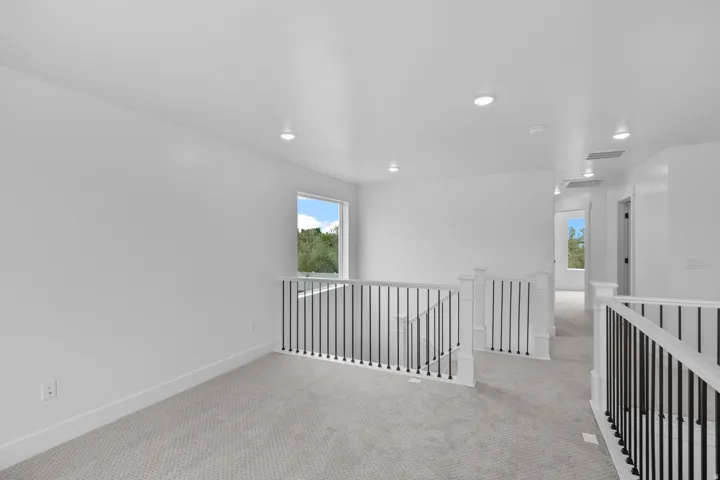Carpeted landing with white walls, recessed lighting, and black metal balusters with white newel posts