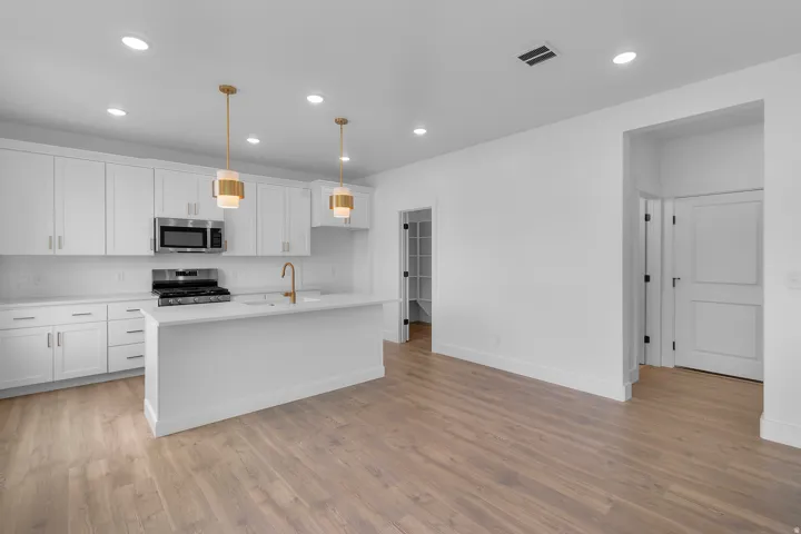 Modern kitchen featuring white cabinetry, a central island with a sink, stainless steel appliances, recessed lighting, and wood-finish flooring