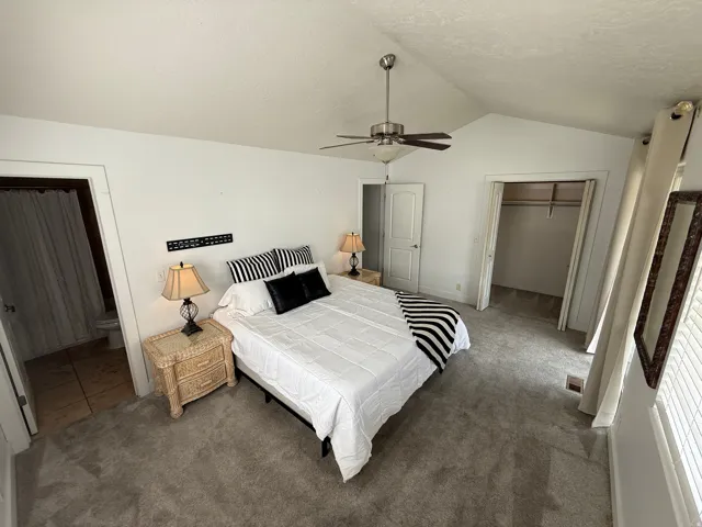 Vaulted ceiling with a ceiling fan, plush carpet flooring, a walk-in closet, and an attached bathroom with tile flooring