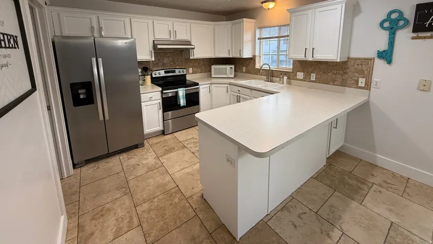Kitchen featuring white cabinetry, stainless steel appliances, light-toned countertops, and large format floor tiling
