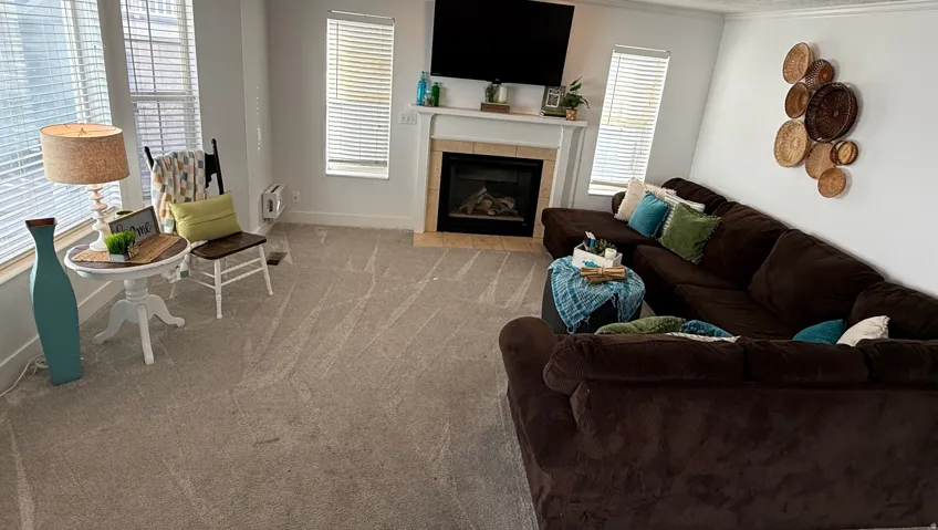 Neutral tone carpeting throughout, a fireplace with a white mantel and tile surround, and multiple windows with blinds