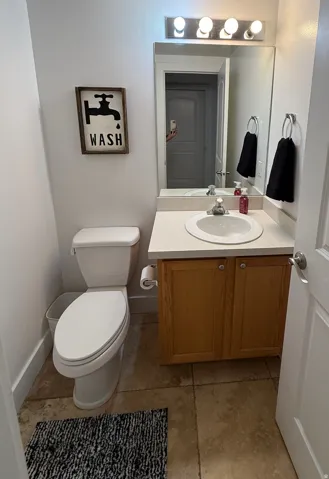 Powder room featuring a single vanity with wood-finish cabinetry, a ceramic basin, and a wall-mounted mirror with overhead lighting