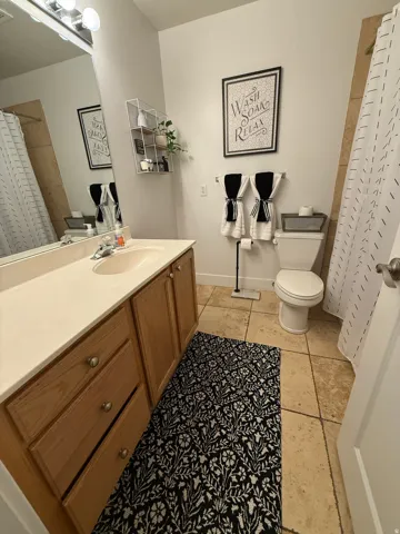 Neutral, well-appointed bathroom featuring wood-finish vanity cabinetry with ample storage, ceramic tile flooring, and dual towel bars
