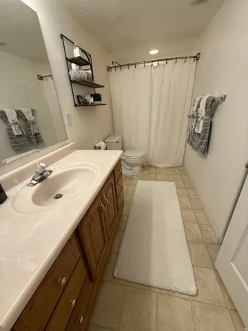Wood-finish vanity with integrated sink and chrome faucet, tile flooring, and wall-mounted shelving