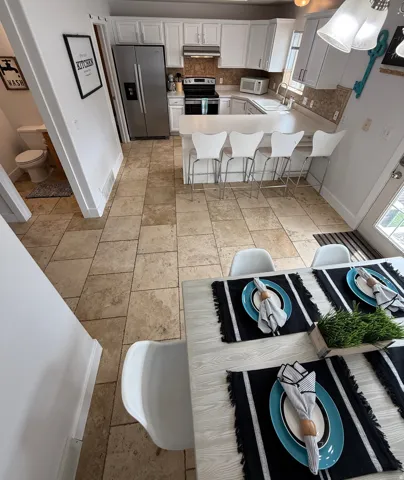 Kitchen featuring white cabinetry, stainless steel appliances, a U-shaped countertop with bar seating, and a tile backsplash