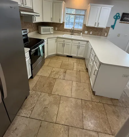 Kitchen featuring white cabinetry, stone tile backsplash, light-toned countertops, stainless steel appliances, and large format floor tiling