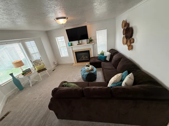 Recessed fireplace with a stone surround and mantle, bay window with multiple panes, light-toned carpeting, crown molding, and a semi-flush mount ceiling light fixture