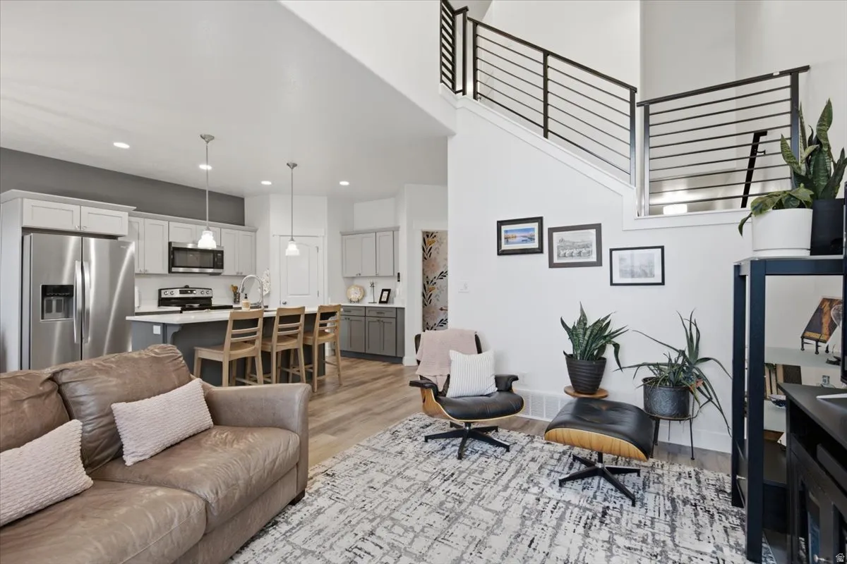 Open-concept living space featuring wood-finish flooring, a kitchen island with seating, stainless steel appliances, and a staircase with contemporary black railings
