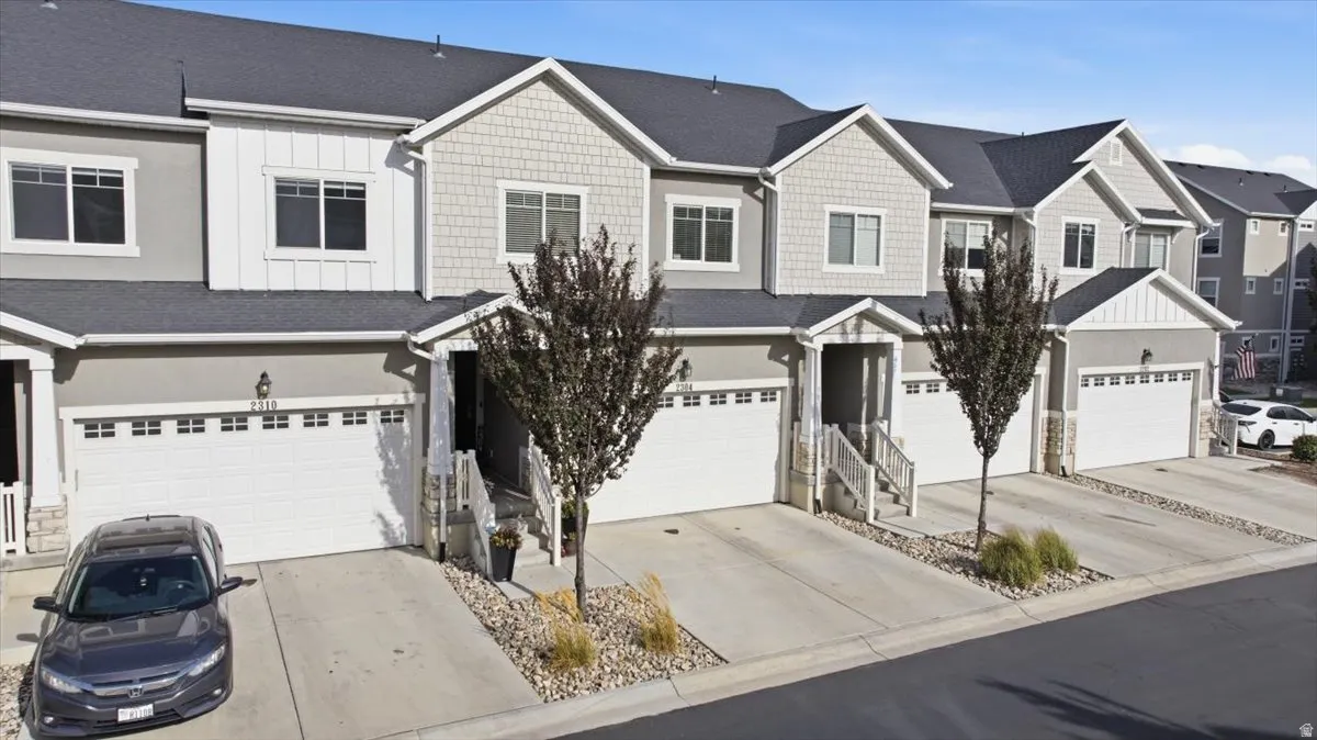 Two-story townhome featuring a two-car garage, stone accents, shingle siding, and a dark shingle roof