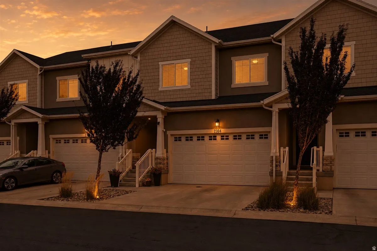 Two-story townhome with attached two-car garage, covered porch entry, and mature landscaping
