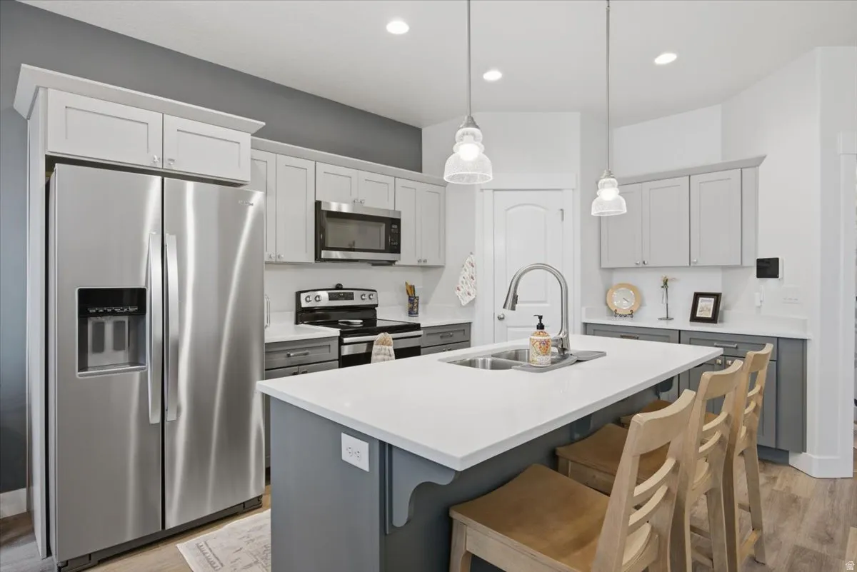 Kitchen featuring stainless steel appliances, light gray upper cabinetry, dark gray lower cabinetry, a center island with a white countertop, and pendant lighting
