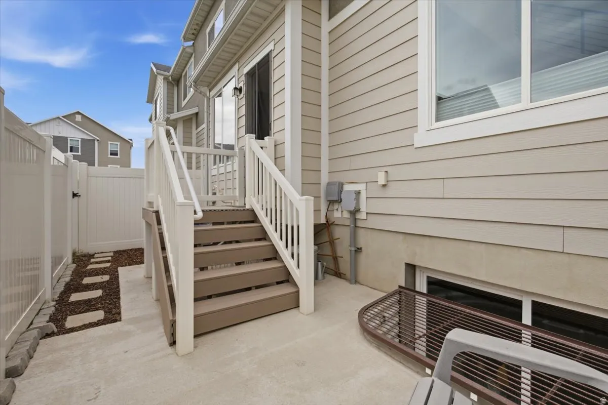 Poured concrete patio, composite deck stairs with white railings, and tan siding