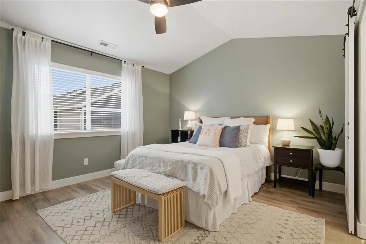 Serene primary bedroom showcasing soft sage-green walls, wood-finish flooring, and abundant natural light from a large multi-pane window