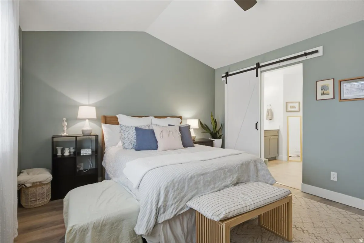 Vaulted ceiling, wood-finish flooring, accent wall, ceiling fan, and barn door entry