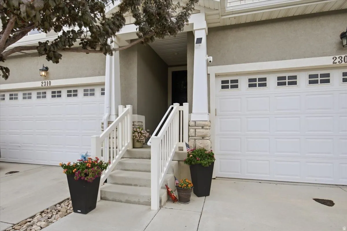 Front entry with white railings, concrete steps, and stone column accents