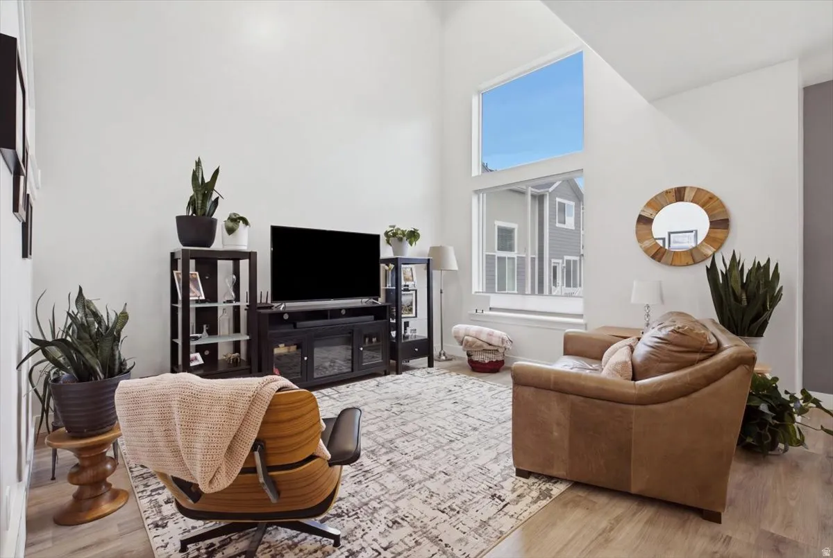 Vaulted ceiling, wood-finish flooring, white painted walls, large picture windows, and built-in media console
