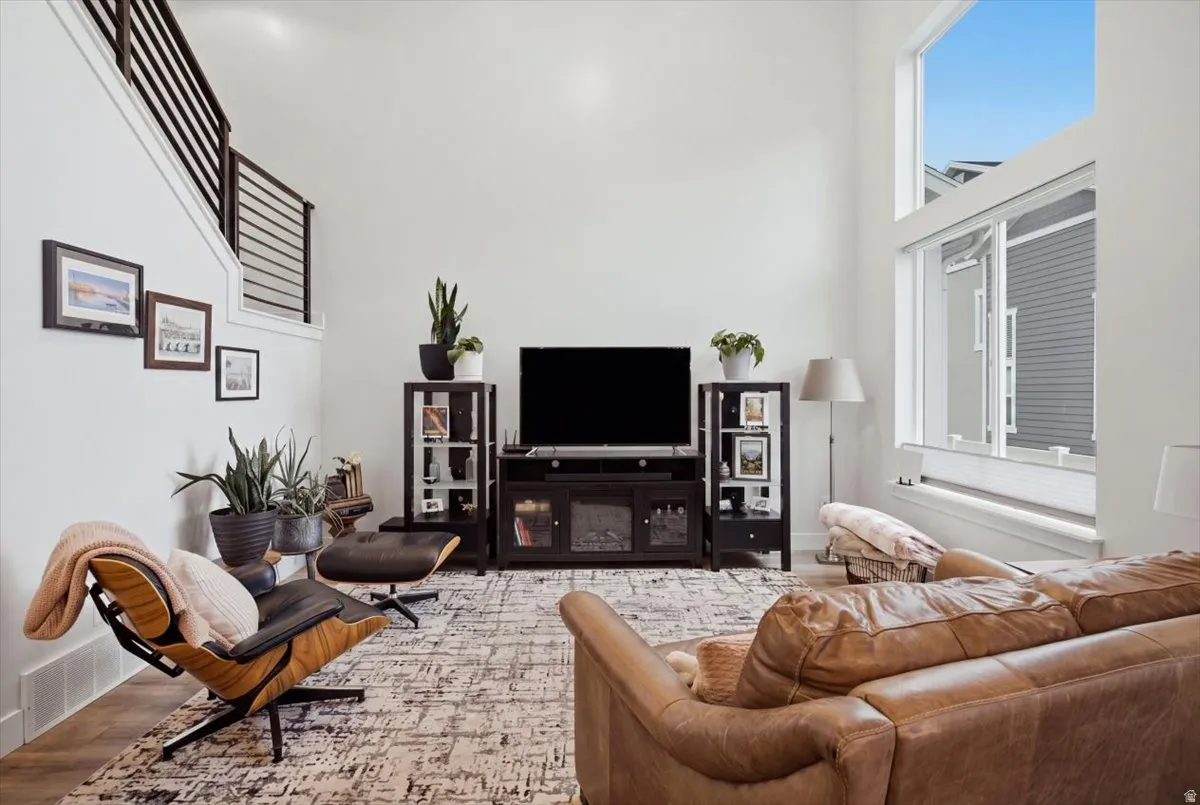 Two-story ceiling, large format windows, wood-finish flooring, white walls, and a staircase with open risers and horizontal railings