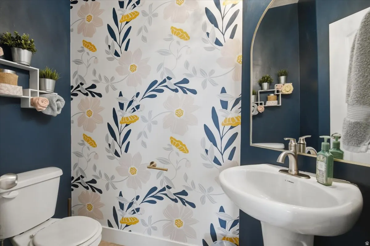 Pedestal sink with brushed nickel faucet, wall-mounted mirror, white toilet, and decorative floral wallpaper