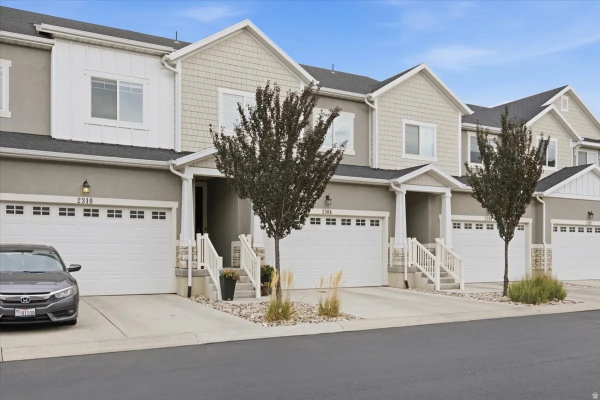 Two-story townhome exterior featuring an attached garage, white railings, and textured siding accents