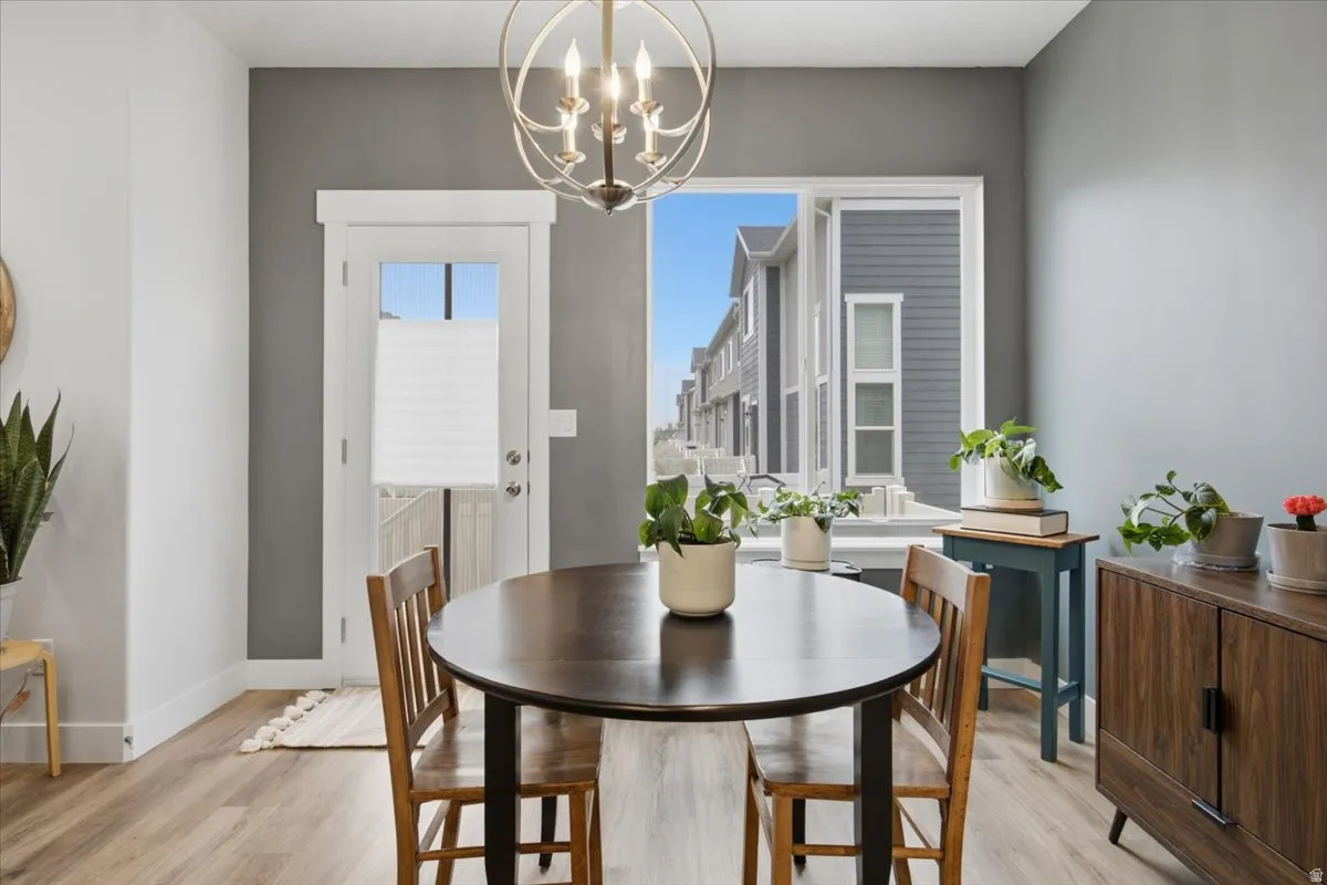 Dining area featuring wood-finish flooring, a white trim door, a large window, and a contemporary chandelier