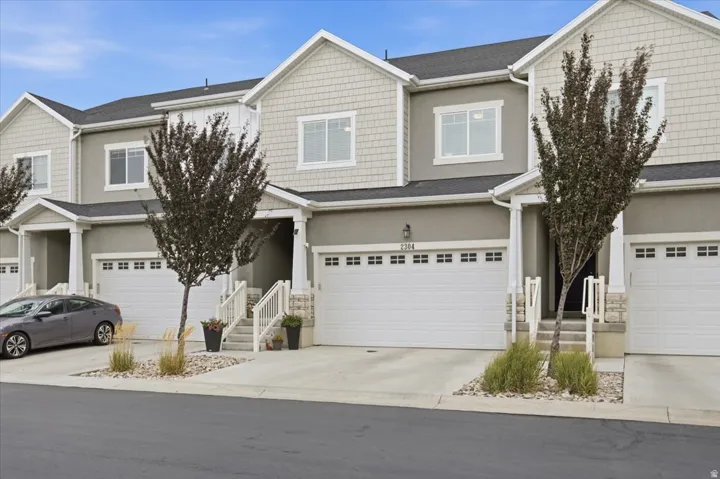 Stucco and shingle-style exterior with white-framed windows, white garage doors with window inserts, and a concrete driveway