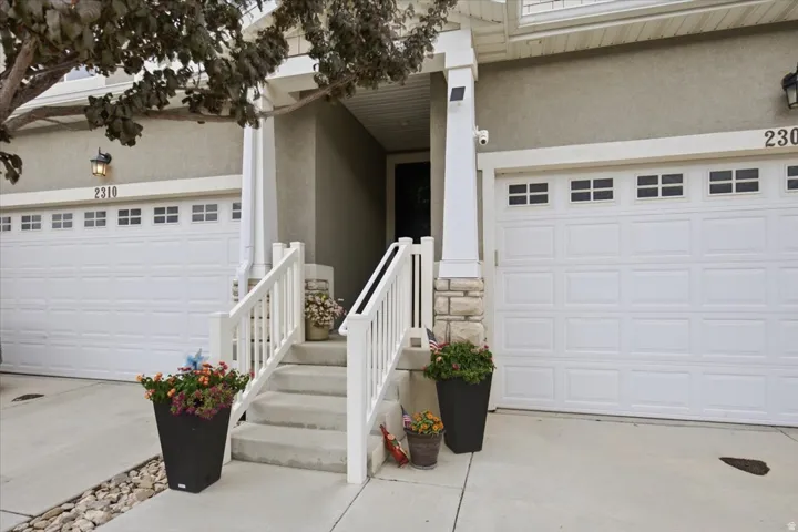 Front entry with white railings, concrete steps, and stone column accents