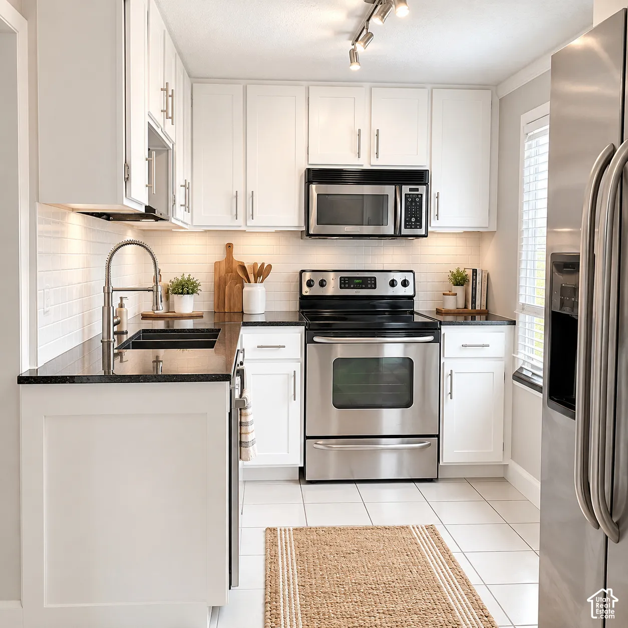 White cabinetry with brushed nickel hardware, stainless steel appliances, black countertops, white subway tile backsplash, and white tile flooring