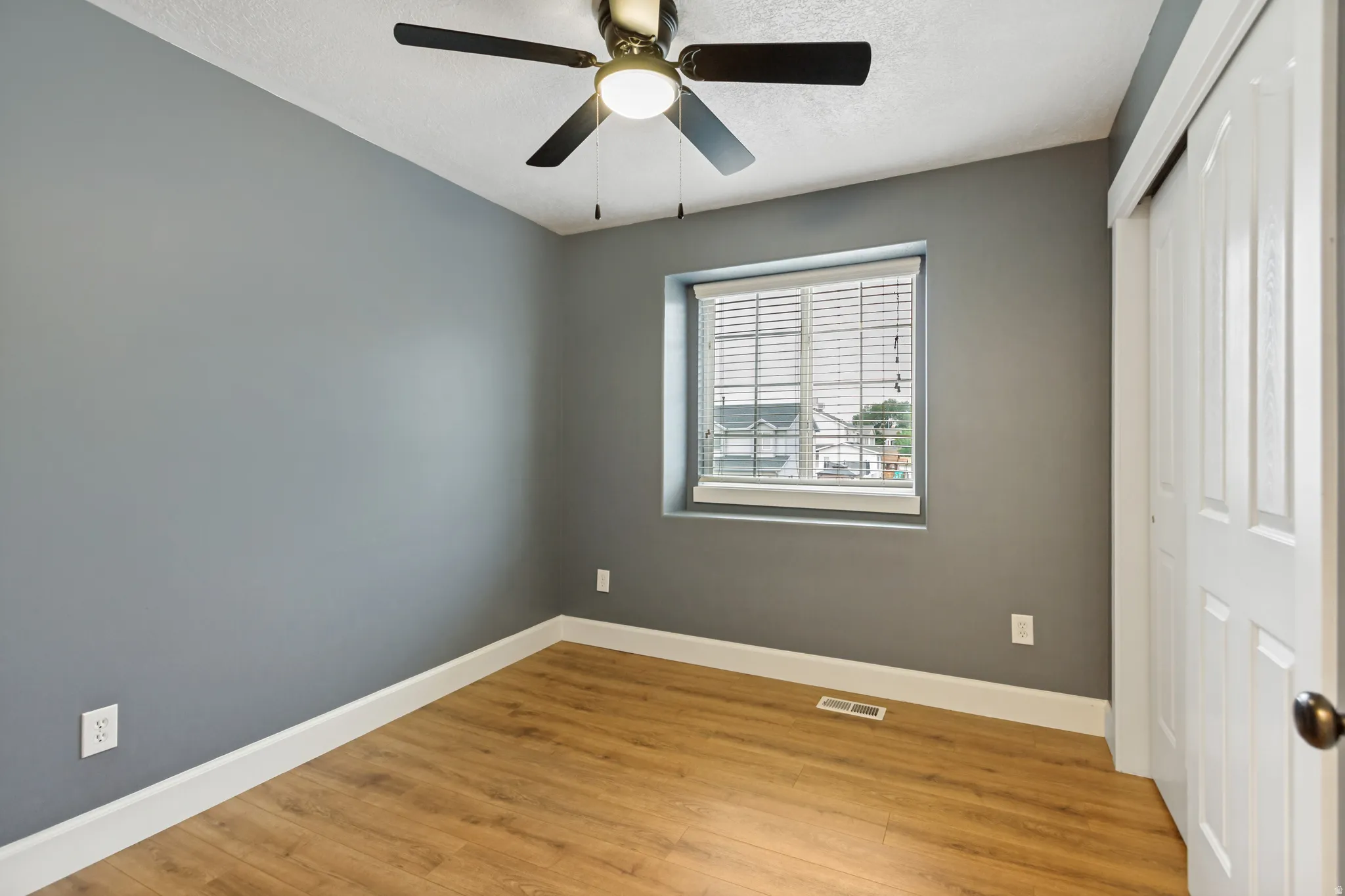 Room featuring wood-finish flooring, a ceiling fan with integrated lighting, a window with blinds, and a bi-fold closet door
