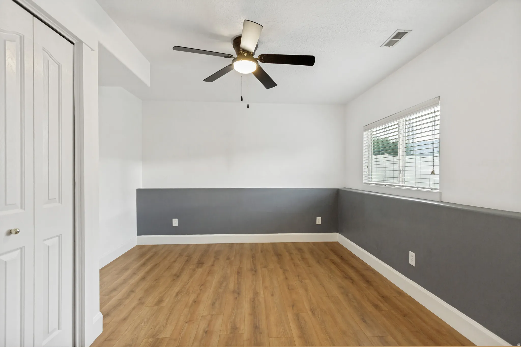 Wood-finish flooring with white trim, a ceiling fan, and window with blinds