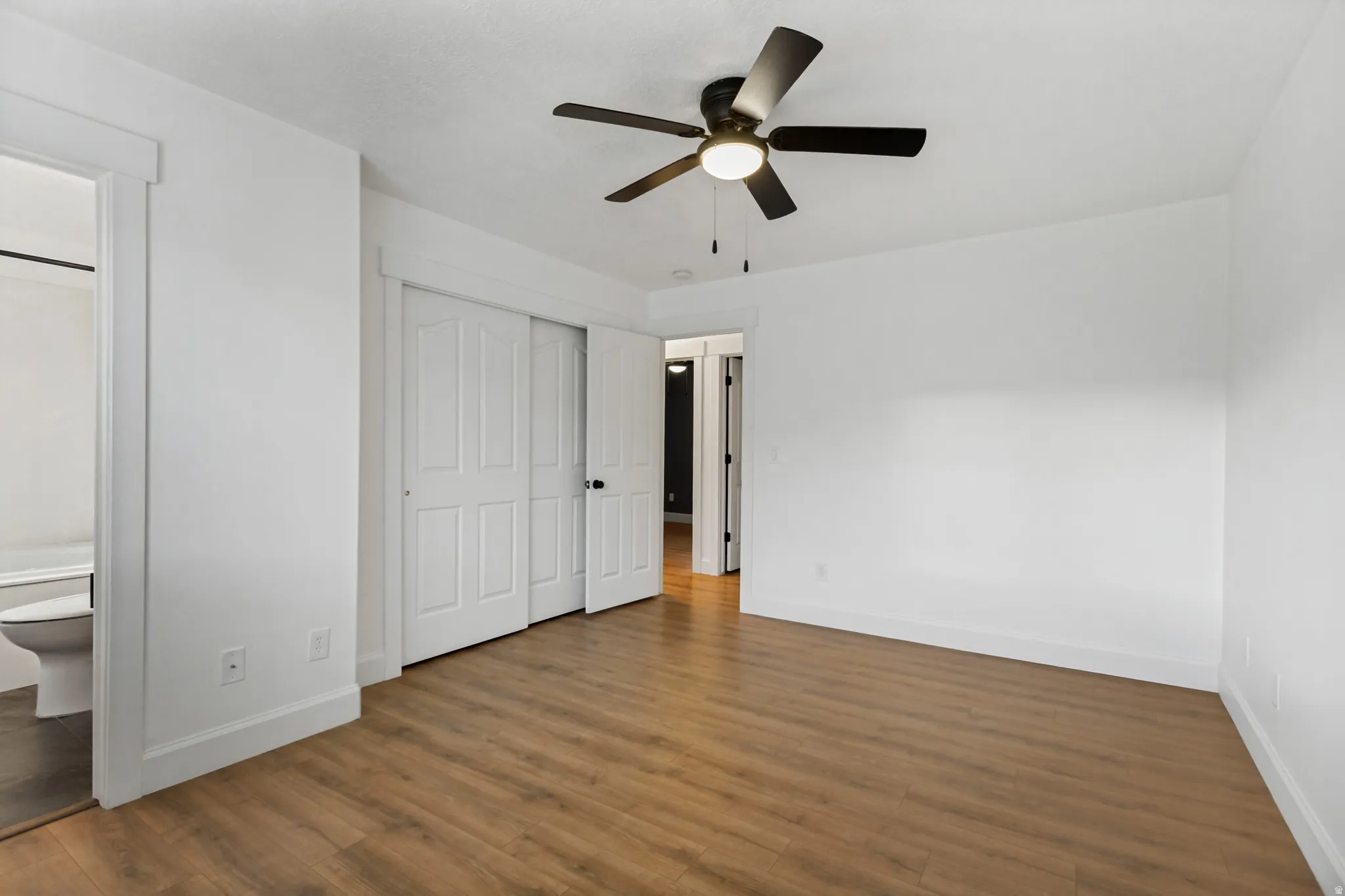Wood-finish flooring with white walls, a ceiling fan with integrated lighting, and a white sliding closet door