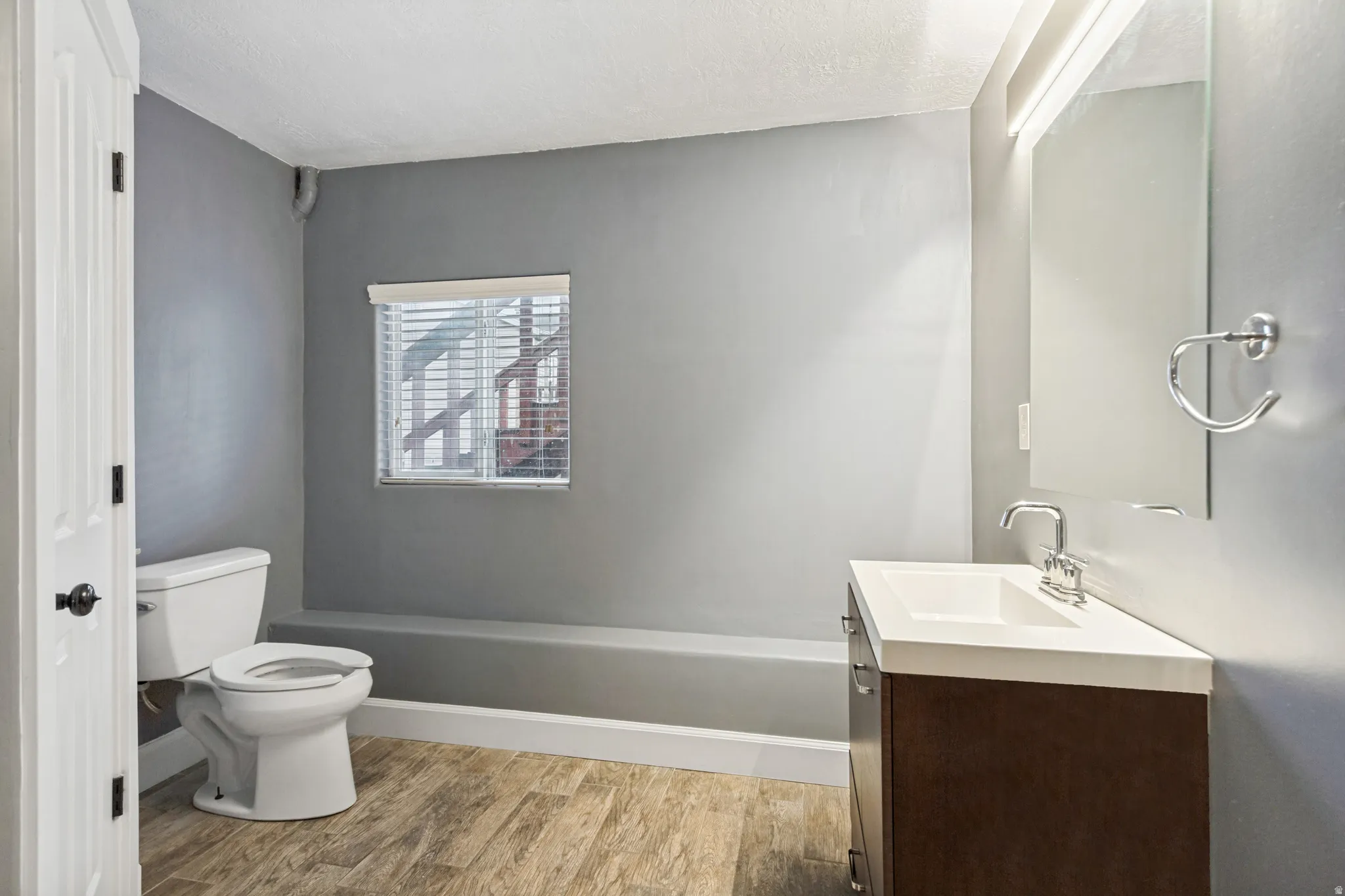 Bathroom featuring wood-finish flooring, a contemporary vanity with an integrated sink, a wall-mounted mirror, and a window with blinds
