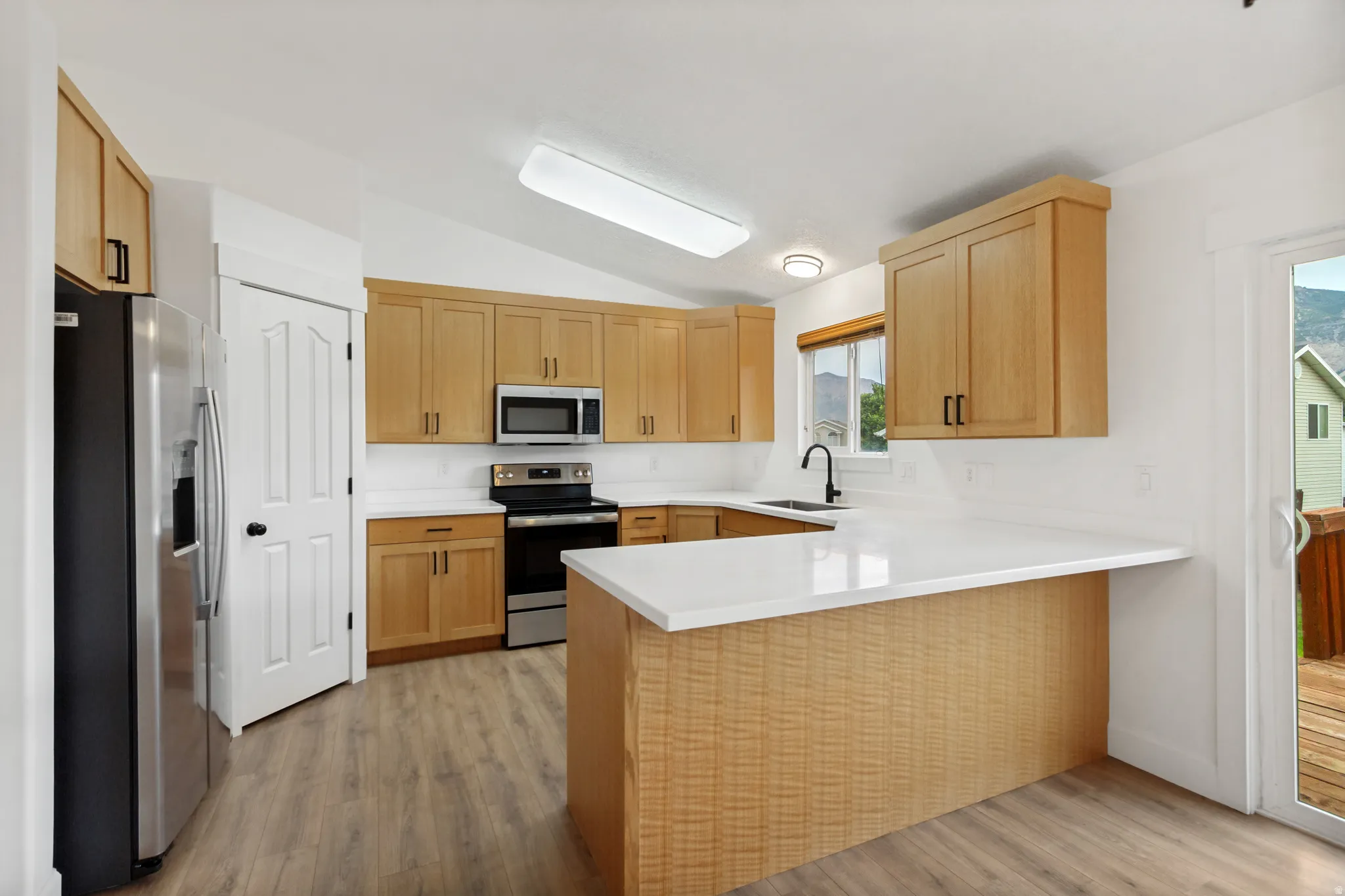 Kitchen featuring wood-finish cabinetry, stainless steel appliances, white countertops, and wood-finish flooring