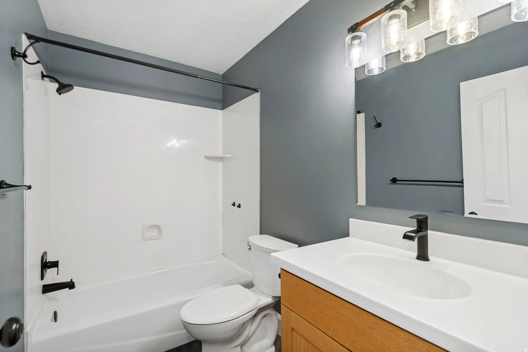 Bathroom featuring a bathtub with an integrated shower, matte black fixtures, wood-finish vanity with an integrated sink, white countertop, and a wall-mounted medicine cabinet
